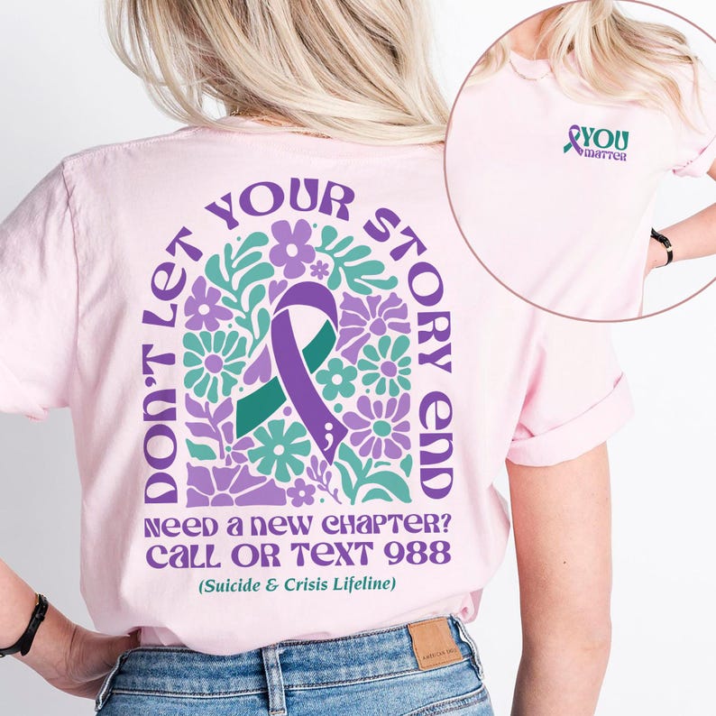 Puede incluir: Camiseta rosa con una cinta morada y un dise&ntilde;o floral en la espalda. El texto dice "No dejes que tu historia termine. &iquest;Necesitas un nuevo cap&iacute;tulo? Llama o env&iacute;a un mensaje de texto al 988 (L&iacute;nea de vida para el suicidio y la crisis)". La parte delantera de la camiseta tiene una cinta morada con el texto "T&uacute; importas".