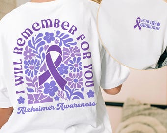 Puede incluir: Camiseta blanca con una cinta morada y un diseño floral en la espalda. El texto "Te recordaré para siempre por la concienciación sobre el Alzheimer" está impreso en la parte posterior de la camiseta. La parte delantera de la camiseta tiene una cinta morada con el texto "Para mi abuela" impreso en ella.