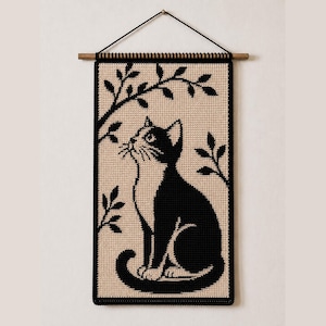 May include: A rectangular wall hanging featuring a black and beige crochet pattern of a cat sitting under a leafy branch. The piece is suspended from a wooden dowel with a black cord, showcasing a detailed two-tone design with a cat looking upward.