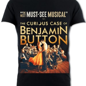 May include: Black t-shirt featuring a gold graphic of a musical production. The graphic depicts a couple dancing with a band playing in the background. The text "The Curious Case of Benjamin Button" is displayed in large gold letters.