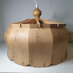 May include: A light-colored, wooden pendant light fixture. The fixture has a rounded, scalloped base and a segmented, ridged top. A wooden sphere and a white cord are attached to the top. The wood grain is visible throughout the fixture.