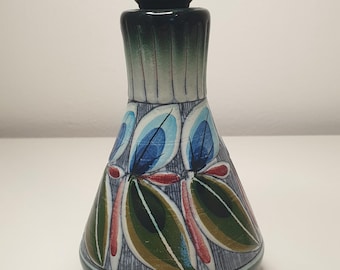 Puede incluir: Una lámpara de mesa de cerámica con un diseño floral verde, azul y rojo. La lámpara tiene un cable negro y un casquillo negro.