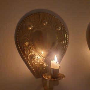 以下が含まれることがあります： ハート型のデザインとキャンドルホルダーが付いた金色の壁掛け照明。キャンドルに火が灯り、炎が見えます。