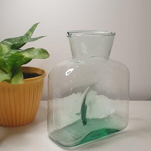 Pode incluir: Uma jarra de vidro transparente com uma base verde. A jarra tem uma boca larga e um corpo arredondado.
