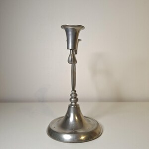 K&ouml;nnte beinhalten: Ein silberfarbener Kerzenhalter mit breitem, kreisf&ouml;rmigem Fu&szlig; und dekorativem Stiel. Die Oberseite hat ein ausgestelltes, becherartiges Design zur Aufnahme einer Kerze. Der Kerzenhalter ist aus Metall und hat eine Vintage-&Auml;sthetik. H&ouml;he ca. 20 cm.