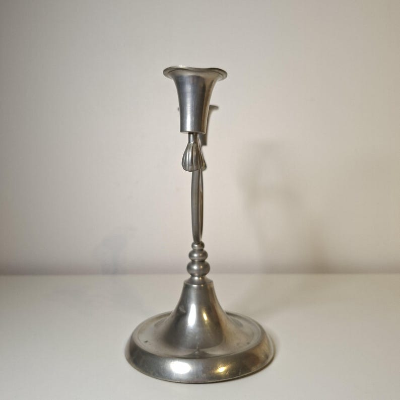 K&ouml;nnte beinhalten: Ein silberfarbener Kerzenhalter mit breitem, kreisf&ouml;rmigem Fu&szlig; und dekorativem Stiel. Die Oberseite hat ein ausgestelltes, becherartiges Design zur Aufnahme einer Kerze. Der Kerzenhalter ist aus Metall und hat eine Vintage-&Auml;sthetik. H&ouml;he ca. 20 cm.