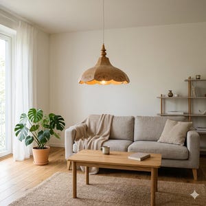 May include: A wooden pendant light with a scalloped shade hangs above a living room. The light fixture is suspended from the ceiling and illuminates the space. The room features a sofa, coffee table, and a potted plant.