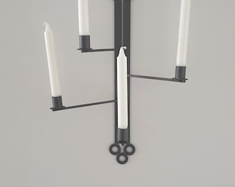 Peut inclure: Un porte-bougie mural en métal noir avec quatre bras, chacun tenant une bougie blanche. Le porte-bougie a un design décoratif en haut et en bas.