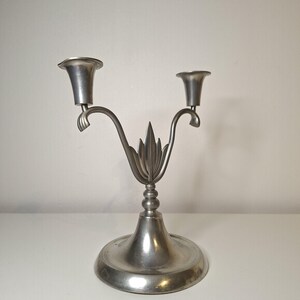 K&ouml;nnte beinhalten: Ein silberfarbener, zweiarmiger Kerzenhalter mit dekorativem Blattdesign. Der Sockel ist rund, und die Arme kr&uuml;mmen sich nach oben, um die Kerzen zu halten. Der Kerzenhalter ist aus Metall und hat eine Vintage-&Auml;sthetik.