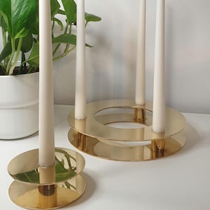 以下が含まれることがあります： 金色の金属製のキャンドルホルダー2個セット。大きなホルダーはキャンドルを3本立てられる円形のデザイン。小さなホルダーはキャンドルを1本立てられる円形のデザインです。