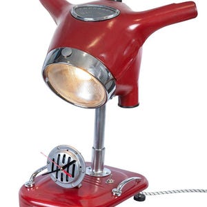 May include: Red and chrome table lamp shaped like a vintage scooter. The lamp has a round headlight, a clock face on the side, and a cord.