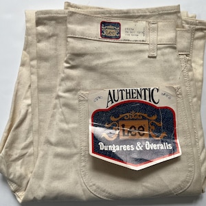 May include: Off-white Lee dungarees and overalls, folded. The pants have a tag that reads "AUTHENTIC Lee Dungarees & Overalls." The tag also shows the size 29x34. The pants are made of 100% cotton.