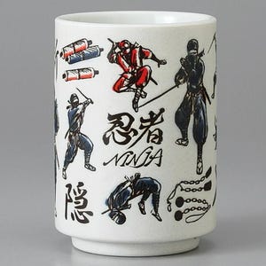 May include: White ceramic mug featuring black and red ninja illustrations and Japanese characters. The mug has a cylindrical shape with a slightly flared base and a white interior.