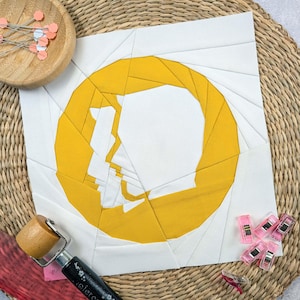 Könnte beinhalten: Ein weißer Stoffquadrat mit einem gelben Kreis in der Mitte. Der Kreis besteht aus vielen kleineren Dreiecken, die ein Spiralmuster bilden. Der Kreis ist ausgeschnitten, um eine Form zu erzeugen, die einem Kopf und Schultern ähnelt.