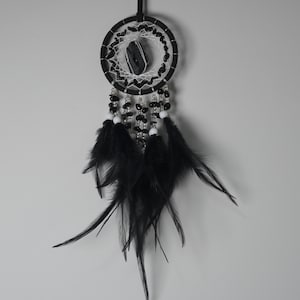 May include: A black and white dreamcatcher with a central stone and hanging feathers. The circular frame is black, with a white web design and black beads. Black feathers hang from the bottom, creating a decorative and spiritual piece.