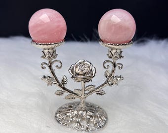 May include: A silver-coloured decorative candle holder with two pink rose quartz spheres. The holder has a floral design with a central rose and branching stems. The spheres are approximately 5 cm in diameter.