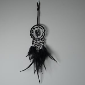 May include: A black and white dreamcatcher with a central stone and hanging black feathers. The dreamcatcher is suspended by a black cord, and features a circular woven web design with black and white beads.