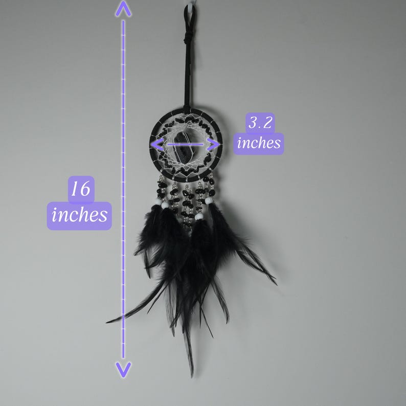 May include: A black dreamcatcher, 16 inches long and 3.2 inches wide, hangs against a gray background. The dreamcatcher features black feathers, beads, and a woven center. The design includes a black cord for hanging.