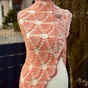 Op de afbeelding: Een gehaakte sjaal in een verloop van roze en wit, getoond op een wit mannequin. De sjaal heeft een delicaat, kantpatroon.