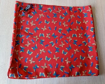 May include: A red silk scarf with a repeating pattern of blue, green, and tan butterflies. The scarf is folded and appears to be new. A small tag in the corner reads "100% Silk".
