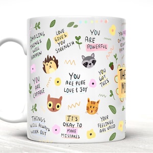May include: White ceramic mug with a colorful design featuring animals, flowers, and positive affirmations. The text includes phrases like "You are powerful", "Love gives you strength", and "Things will always work out".
