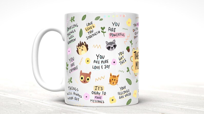 May include: White ceramic mug with a colorful design featuring animals, flowers, and positive affirmations. The text includes phrases like "You are powerful", "Love gives you strength", and "Things will always work out".