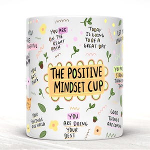 May include: White ceramic mug with a colorful design featuring the text "The Positive Mindset Cup" and various positive affirmations, including "You are on the right path", "Today is going to be a great day", and "You are doing your best".