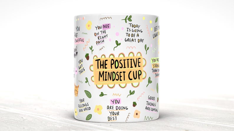May include: White ceramic mug with a colorful design featuring the text "The Positive Mindset Cup" and various positive affirmations, including "You are on the right path", "Today is going to be a great day", and "You are doing your best".