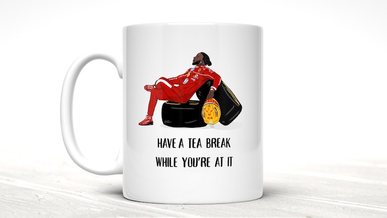 May include: White ceramic mug with a humorous illustration of a person in a red racing suit, resting on a tire and helmet. The text "HAVE A TEA BREAK WHILE YOU'RE AT IT" is printed below the image.