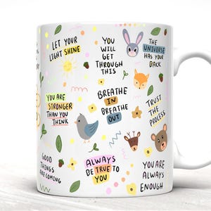 May include: White ceramic mug with a colorful design featuring various animals, flowers, and inspirational quotes. The quotes include "Let your light shine", "You will get through this", "Breathe in breathe out", "The universe has your back", "Trust the process", "Good things are coming", "Always be true to you", and "You are always enough".