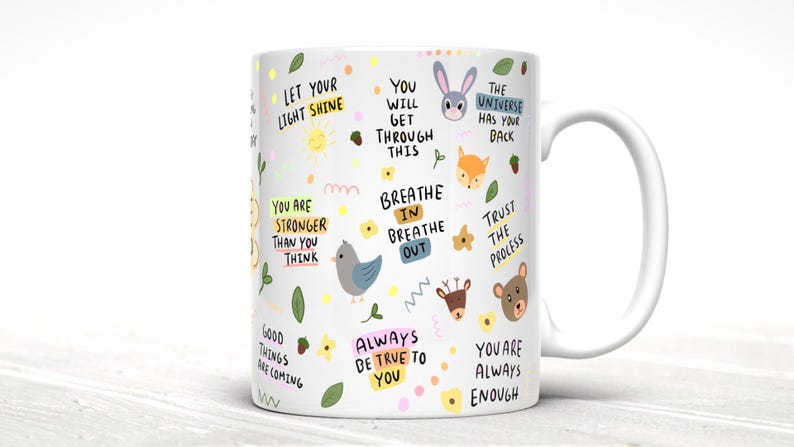May include: White ceramic mug with a colorful design featuring various animals, flowers, and inspirational quotes. The quotes include "Let your light shine", "You will get through this", "Breathe in breathe out", "The universe has your back", "Trust the process", "Good things are coming", "Always be true to you", and "You are always enough".