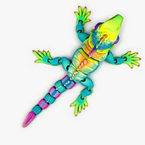 May include: A multi-colored, articulated lizard figurine featuring a gradient of bright yellow, orange, blue, and purple hues. The toy has a textured, segmented body, a long tail, and four sprawling legs with detailed toes, all captured from a top-down perspective.