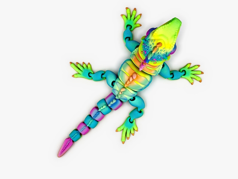 May include: A multi-colored, articulated lizard figurine featuring a gradient of bright yellow, orange, blue, and purple hues. The toy has a textured, segmented body, a long tail, and four sprawling legs with detailed toes, all captured from a top-down perspective.