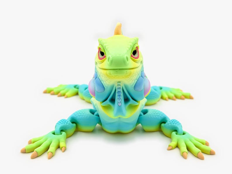 May include: A multi-colored articulated iguana figurine featuring a gradient of lime green, bright yellow, and cyan blue. The lizard has a textured, scaly surface, a prominent dewlap under its chin, and articulated limbs with clawed feet.
