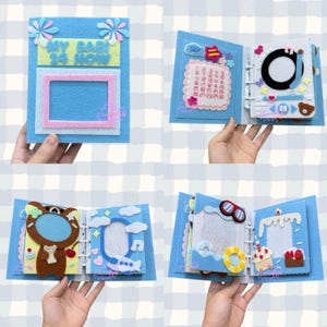 Puede incluir: Un álbum de fotos artesanal de fieltro azul con varios elementos decorativos. El álbum presenta un marco, un calendario y páginas temáticas con un oso, un avión y otros diseños. El texto "MY BABI 24 NOW" es visible.