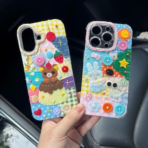 May include: Two colorful, handmade phone cases. One features a bear on a dessert, the other a bunny and cat. Both cases have button and felt embellishments, with patchwork designs in various colors including blue, yellow, and pink.