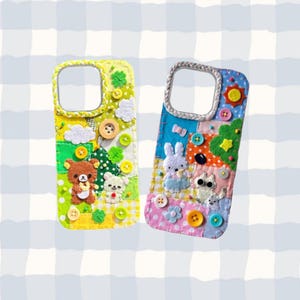 May include: Two colorful, handmade phone cases. One is yellow with a bear and other characters, the other is blue with a bunny and other characters. Both cases have button and felt details.