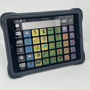 May include: A black tablet with a protective case, displaying a communication app interface. The screen features colorful buttons with icons and text, including "Speak," "Keyboard," and "Home Page." The tablet is designed for augmentative and alternative communication.