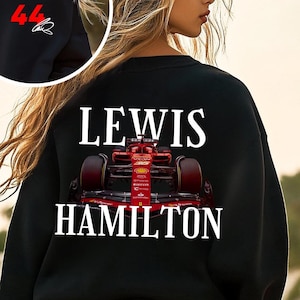 Peut inclure: Sweat-shirt noir avec un motif blanc d'une voiture de course rouge et le texte "LEWIS HAMILTON" au dos. Le devant du sweat-shirt porte le numéro "44" en rouge avec une signature.