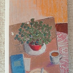 May include: An artistic greeting card featuring a still life scene. A red pot with a green plant sits on a white plate. A blue book, a cup of coffee, and a plate with a knife are also on the table. The background has a wood-like texture.