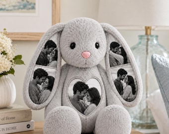 May include: A plush gray rabbit stuffed animal featuring a pink nose and black eyes. The rabbit has three heart-shaped photo inserts: one on each long ear and one on the center of its chest, each displaying a black and white photograph of a couple.