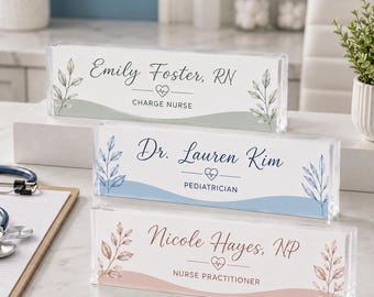 May include: Three rectangular clear acrylic desk nameplates with rounded edges. Each features a printed name, professional title, a small heart with an EKG line, and botanical leaf illustrations in sage green, blue, and dusty rose color schemes.