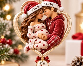 May include: A heart-shaped Christmas ornament featuring a couple wearing Santa hats labeled Sophia and William. The woman wears a heart-patterned outfit, and the man wears a red hoodie and plaid pants. A small circular tag below reads 2026 with footprints.