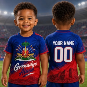 May include: A blue and red t-shirt featuring the Haitian coat of arms and the text "Grenadye Alaso" on the front. The back of the shirt displays "YOUR NAME" above the number "00". The shirt is worn by a young child.