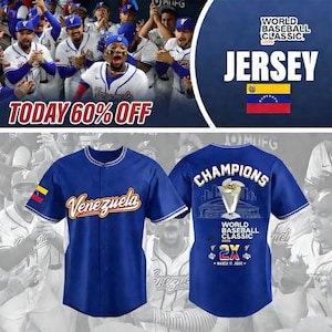 Könnte beinhalten: Blaues Baseball-Trikot mit dem Wort "Venezuela" in goldener Schrift auf der Vorderseite. Das Trikot hat weiße Verzierungen und einen venezolanischen Flaggenaufnäher am Ärmel. Auf dem Rücken steht "CHAMPIONS" mit einer Trophik.