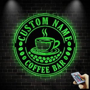 May include: A neon green "Custom Name Coffee Bar" sign. The sign is circular with a coffee cup and coffee beans design. The sign is on a black brick wall. A remote control is in the bottom right corner.