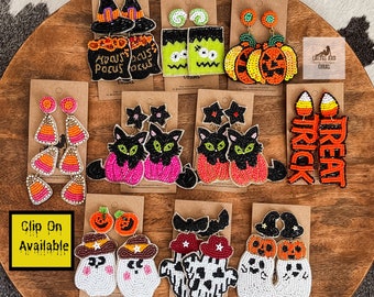 May include: Assortment of Halloween-themed beaded earrings.  The earrings feature various designs including pumpkins, ghosts, cats, candy corn, and witches hats.  The text "Clip On Available" is visible in the image.