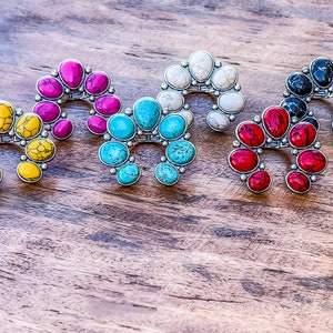 May include: Six colorful rings with a horseshoe shape, each ring is made of silver and has a different colored stone. The stones are turquoise, yellow, pink, red, white, and black.