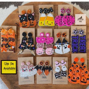 May include: A collection of beaded Halloween earrings in various designs, including cats, candy corn, pumpkins, ghosts, bats, and the words "Trick or Treat." The earrings are displayed on brown cards, with a yellow square that says "Clip On Available."