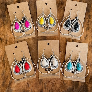 May include: Six pairs of silver hoop earrings with teardrop-shaped turquoise, red, white, black, yellow, and pink stones. All the earrings are the same size and shape, and are set in a silver hoop.